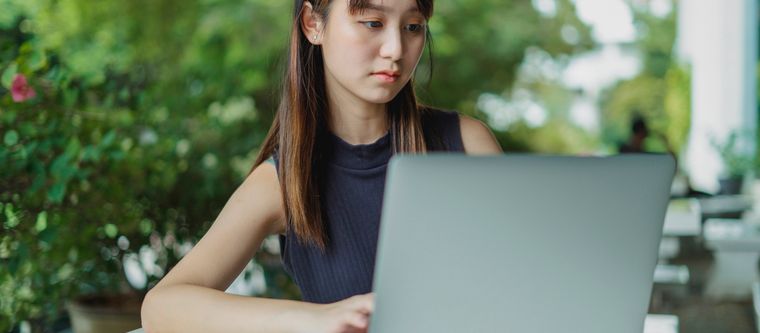 A young woman focused on her laptop, learning something new in warm daylight.