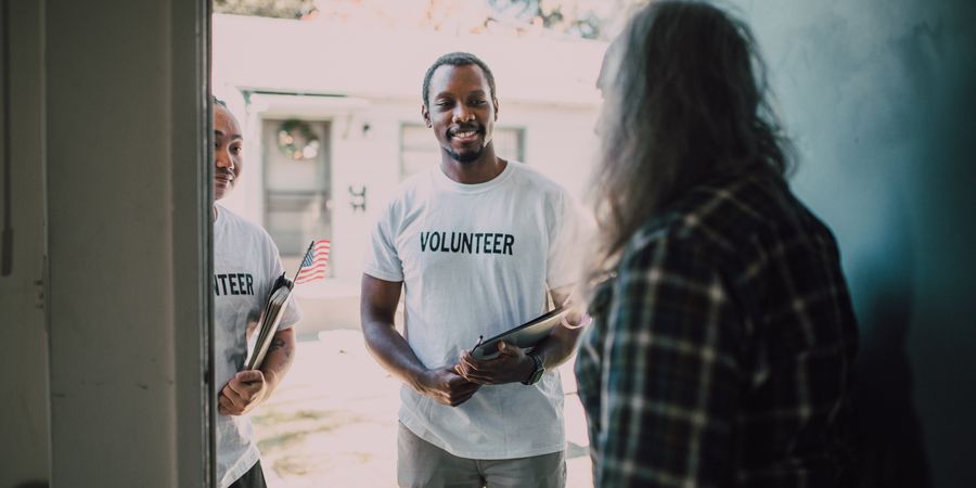 Smiling volunteers in "volunteer" shirts welcoming someone during a community visit.