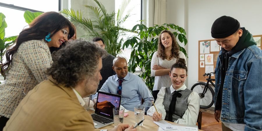 A diverse team collaborating warmly around a table with laptops and plants.